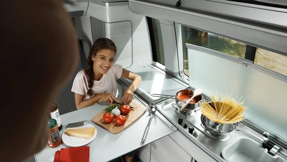 A woman and a girl chopping up some tomatoes inside of a campervan kitchen.