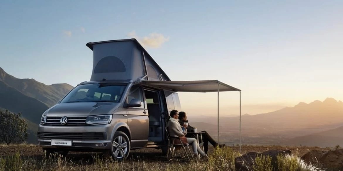 A VW campervan with a canopy extended out on a mountain range.