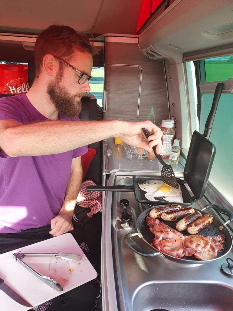 A man cooking a fry up on his campervan cooker.