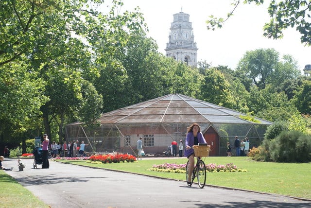 A scenic photo of a woman cycling down a road in a park.