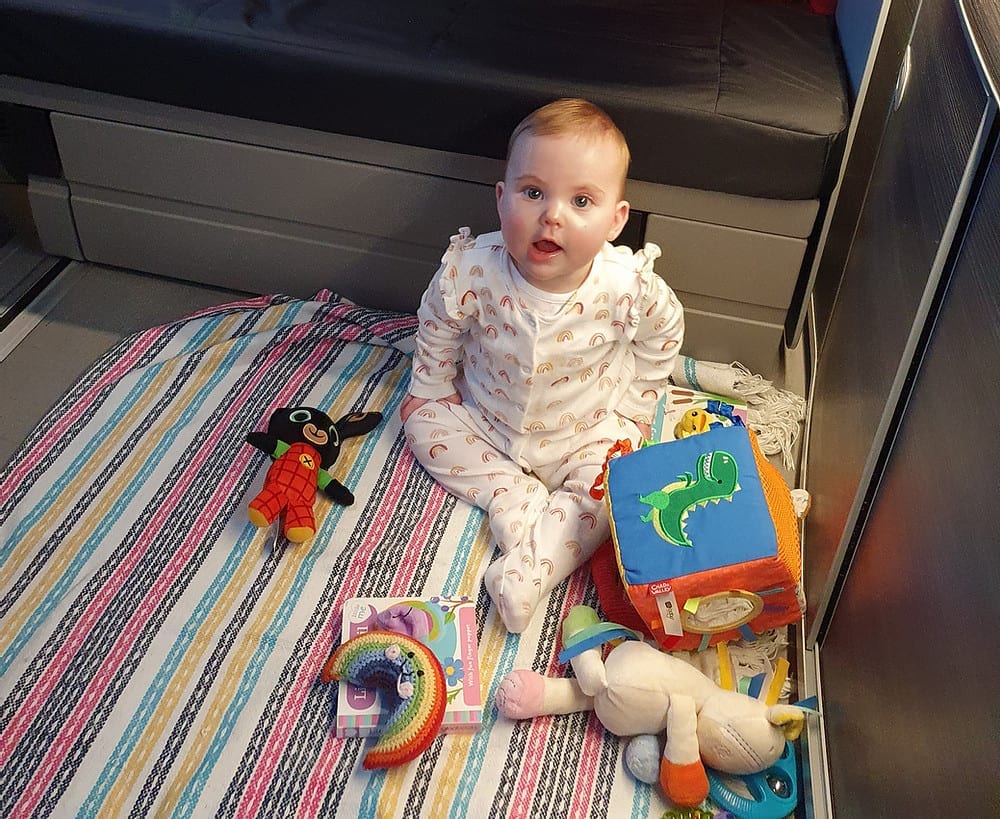 A baby playing with their toys on the floor of a VW campervan