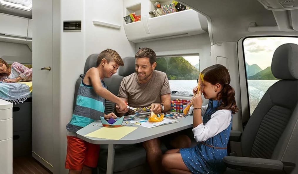 A father and 2 children eating around the pull out table inside of a VW Grand California.