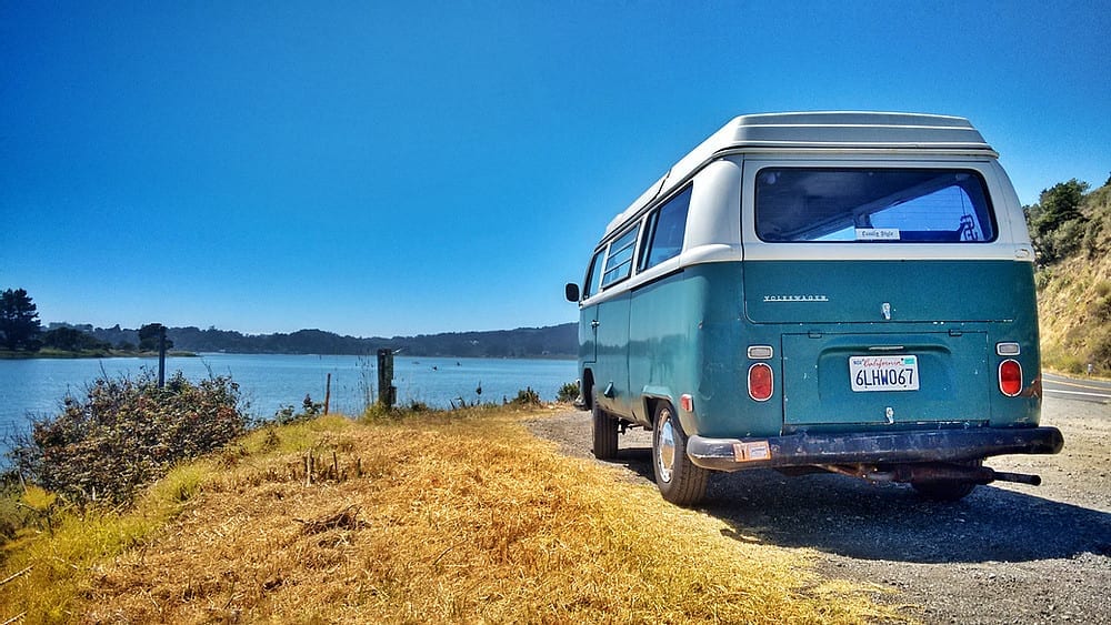 An old VW campervan parked up in front of a scenic lake view.