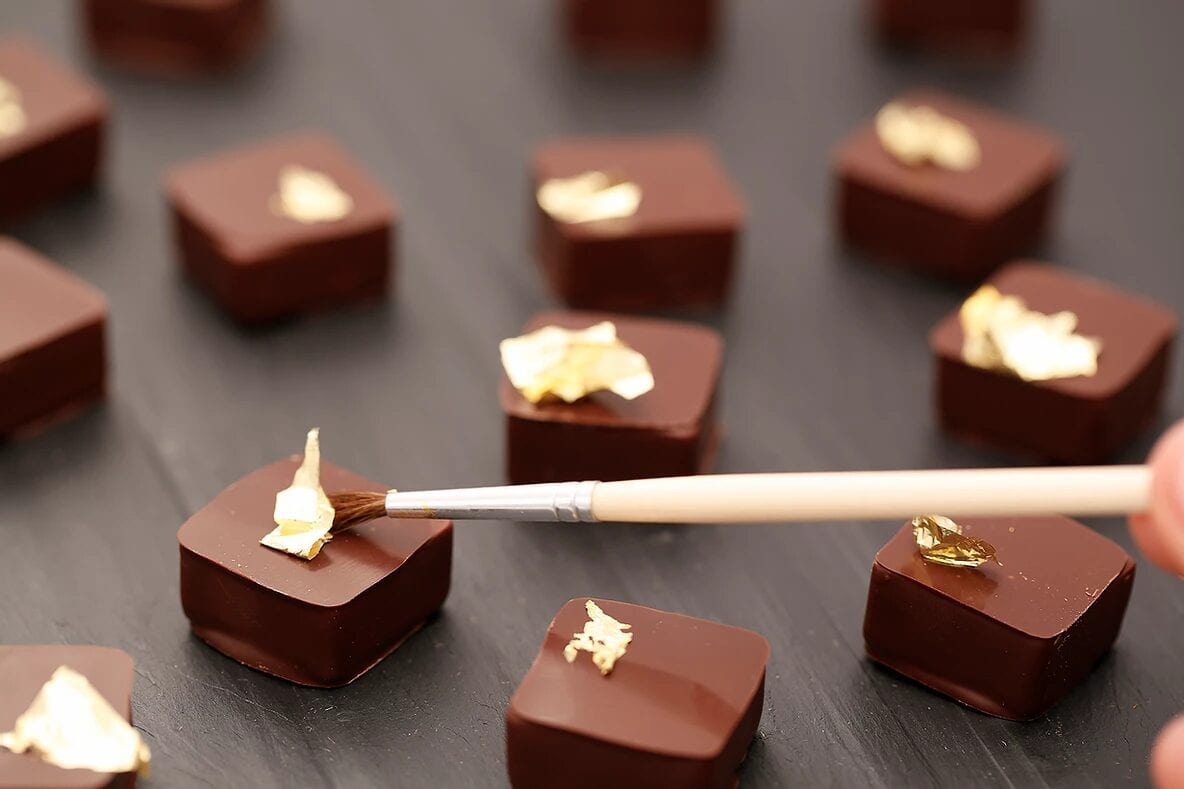 A close up photo of some fancy chocolates being painted gold.