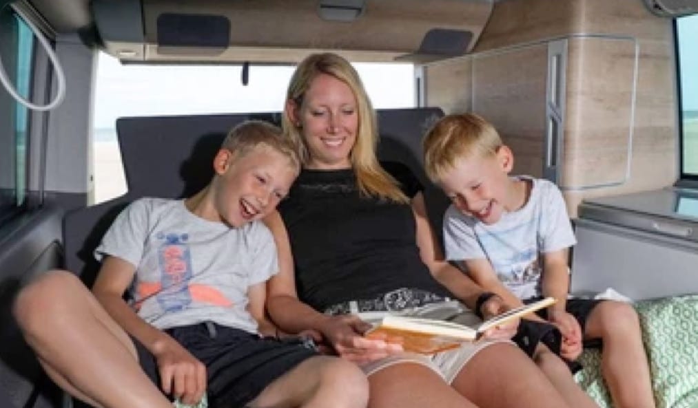 A woman and 2 children having a laugh inside of a VW campervan.