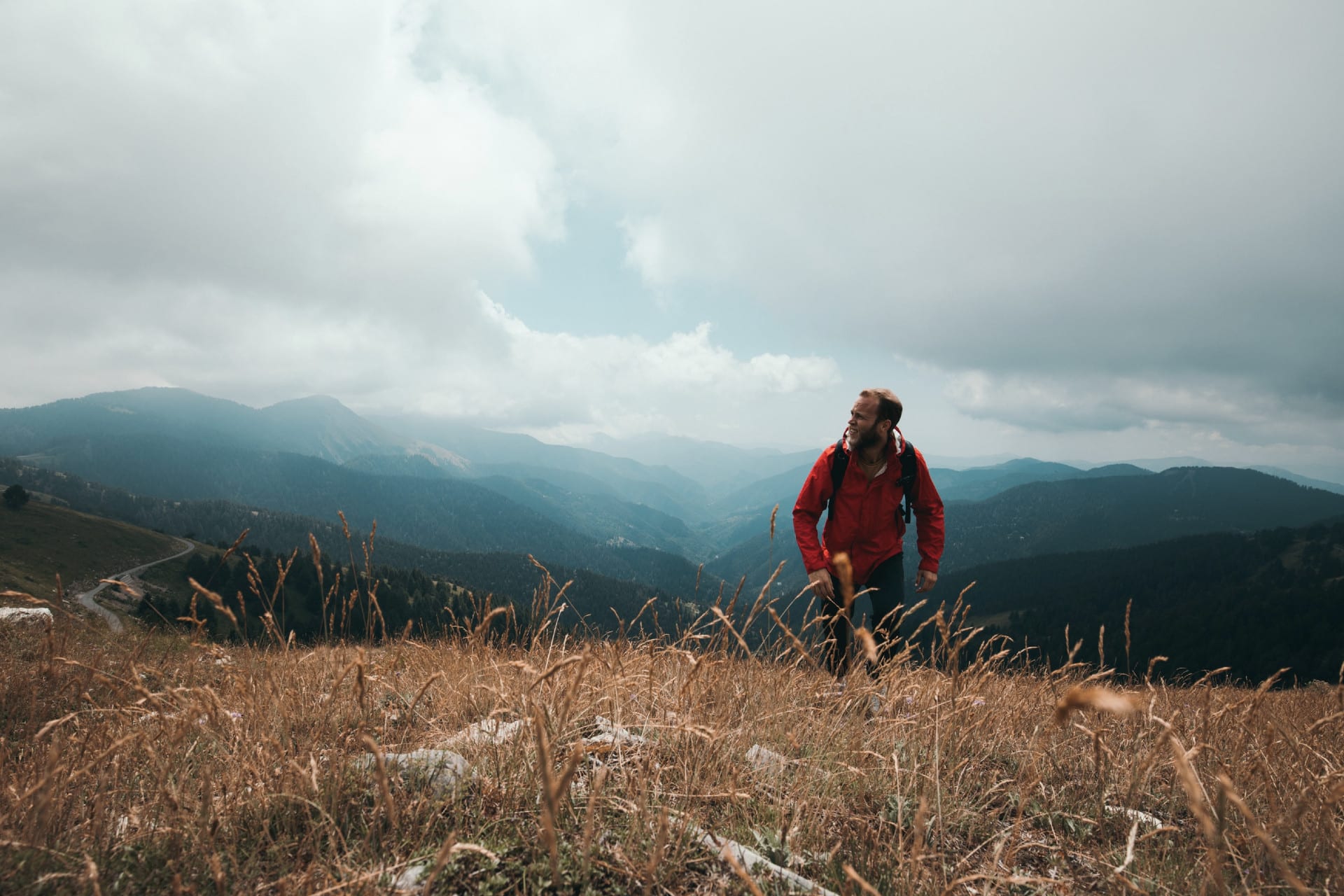 A man in a red coat, hiking up a mountain range.
