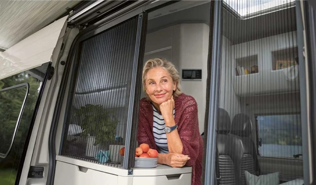 An elderly lady looking outside through a window of the campervan.